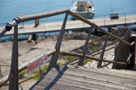 Téléchargez les photos : Un gros plan de panneau d'embarquement italien avec flèche de direction sur la clôture de l'escalier en bois près de la mer - en image libre de droit
