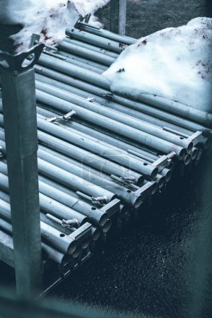 Photo for A vertical shot of the snow-covered stainless steel pipes stacked on top of each in the outside - Royalty Free Image
