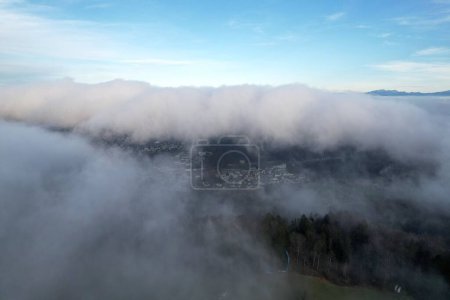 Foto de Una toma aérea de una ciudad y abetos cubiertos de niebla bajo el cielo azul - Imagen libre de derechos