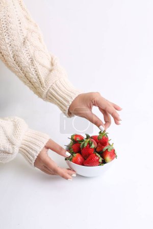 Téléchargez les photos : Plan vertical d'une main cueillant des fraises dans un bol blanc sur une surface blanche - en image libre de droit