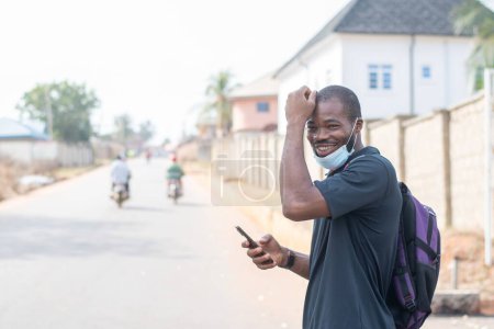 Photo for African man with face mask using his phone outside - Royalty Free Image
