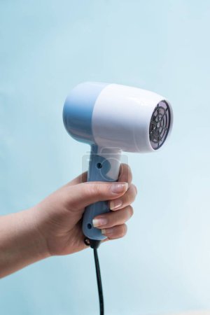 Foto de Un primer plano vertical de una mano sosteniendo un secador de pelo azul delante de un fondo azul - Imagen libre de derechos