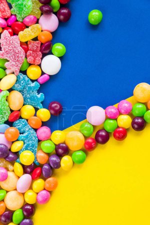 Foto de Un plano vertical de dulces dulces coloridos sobre la mesa sobre un fondo azul y amarillo - Imagen libre de derechos