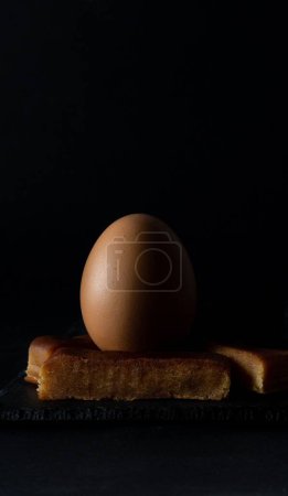 Foto de Una foto vertical de primer plano de un huevo sobre un turrón de yema tostado con fondo negro - Imagen libre de derechos