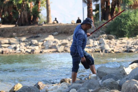 Téléchargez les photos : Un pêcheur caucasien marche pieds nus à travers les rochers sur la jetée à Kineret, Tibériade, Israël. - en image libre de droit