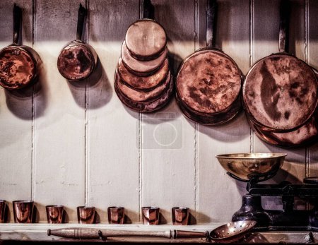 Foto de Una serie de ollas y sartenes inglesas de cobre colgaron en una cocina vintage - Imagen libre de derechos