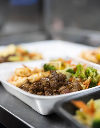 Foto de Una toma vertical de una lonchera con carne asada, ensalada y camarones sobre la mesa - Imagen libre de derechos