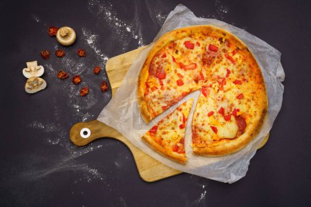 Foto de Una vista superior de una pizza colocada en un papel y tabla de cortar, setas y decoraciones de tomate - Imagen libre de derechos