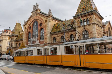 Foto de Un primer plano en ángulo bajo de un tren amarillo frente al Central Market Hall en Budapest, Hungría - Imagen libre de derechos