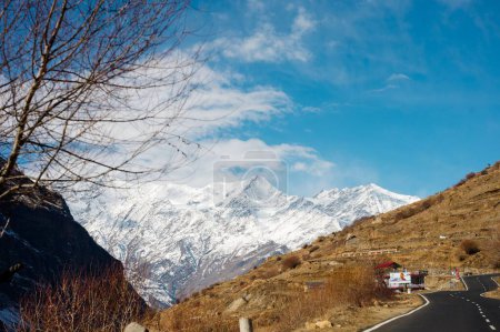 Foto de Escénica vista de invierno desde el camino de asfalto en las montañas cubiertas de nieve y árboles en el lado de la carretera sobre un fondo de cielo azul y nubes - Imagen libre de derechos