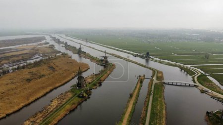 Téléchargez les photos : Vue aérienne des moulins à vent de Kinderdijk et d'un pont sur une rivière par temps brumeux - en image libre de droit