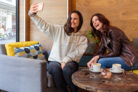 Téléchargez les photos : Deux femmes caucasiennes assises dans un café prenant un selfie - en image libre de droit