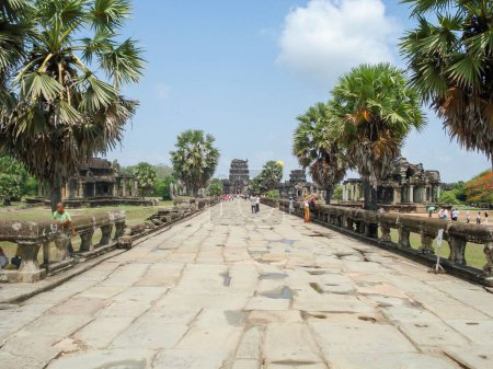 Téléchargez les photos : Une image d'un chemin avec des touristes, avec des palmiers asiatiques des deux côtés et un temple au bout du chemin à Angkor Wat, Cambodge - en image libre de droit