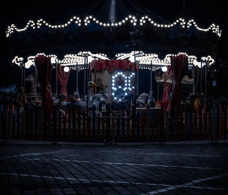 Photo for A carousel in an amusement park for children at Christmas with lights and some people around - Royalty Free Image