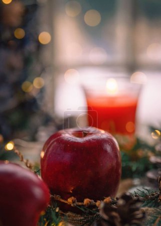 Téléchargez les photos : Un plan vertical d'une pomme rouge avec une bougie en arrière-plan et des lumières de Noël - en image libre de droit