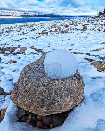 Photo for A closeup shot of a stone covered by snow, on a rocky and snowy coast, with a sea surface and Mount Hood in Oregon in the background - Royalty Free Image