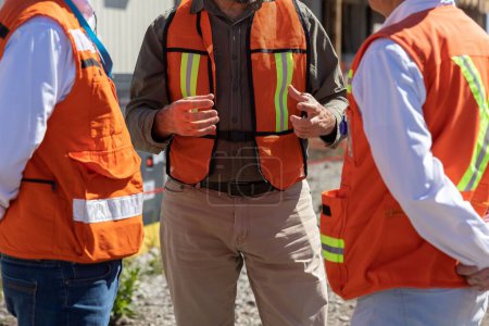 Photo for A closeup of engineers in orange vests at a meeting before working in the field - Royalty Free Image