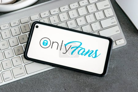 Foto de Un plano de un teléfono inteligente con un logotipo de OnlyFans en él contra un teclado blanco y una mesa gris - Imagen libre de derechos