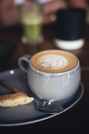 Photo for A vertical shot of a cappuccino served on a plate with a freshly baked biscuit - Royalty Free Image