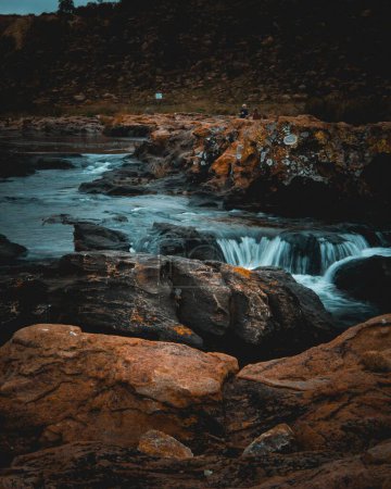 Téléchargez les photos : Une verticale d'une cascade qui coule à travers les roches lors d'une journée nuageuse photographiée en longue exposition - en image libre de droit