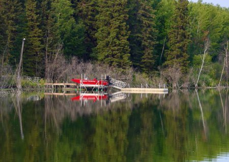 Téléchargez les photos : Un bateau de sauvetage rouge avec des arbres reflétés dans l'eau un jour d'été - en image libre de droit