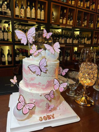 Téléchargez les photos : Un plan vertical de gâteau vanille anniversaire à deux niveaux décoré de papillons roses et nom Joey sur la base - en image libre de droit