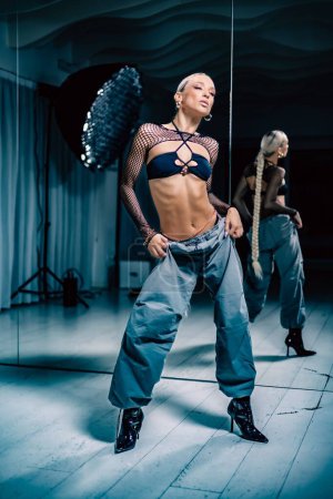 Téléchargez les photos : Vue verticale d'une jolie danseuse Stiletto posant devant le miroir dans un studio - en image libre de droit