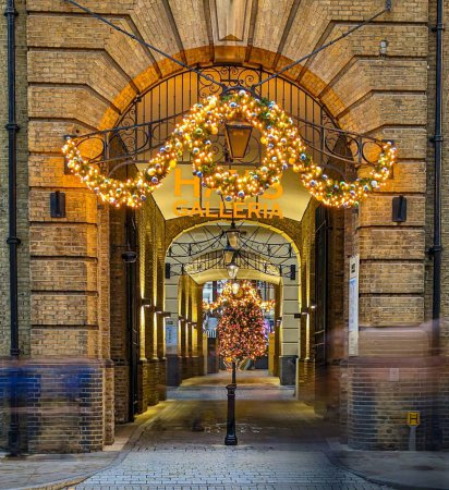 Photo for A vertical shot of a stone arch gate with illuminating Christmas lights hanging in the street - Royalty Free Image