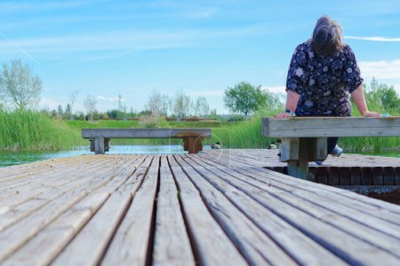 Téléchargez les photos : Femme assise sur un banc sur un quai du lac regardant le ciel bleu - en image libre de droit