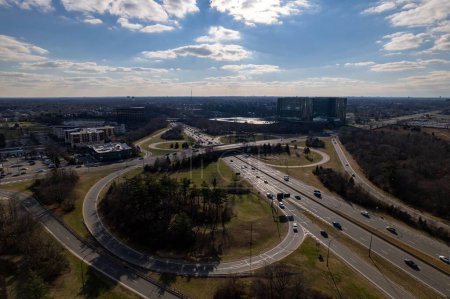 Foto de Una vista aérea de un bucle de carretera en Long Island con árboles verdes, paisaje urbano en el fondo, en un día soleado con nubes en el cielo - Imagen libre de derechos