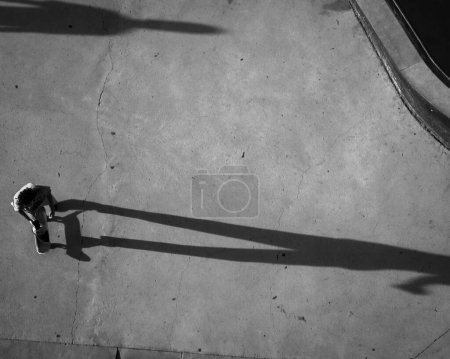 Téléchargez les photos : Un plan en niveaux de gris de drone du patineur TX au skate park jetant une ombre longue dans la ville d'Austin - en image libre de droit