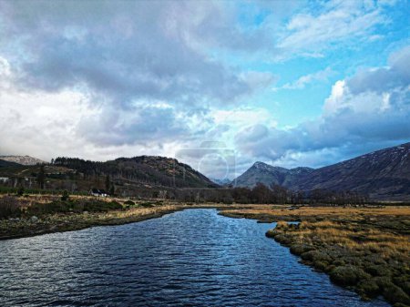 Foto de Un pintoresco plano de un río que fluye a través de las tierras altas escocesas bajo el cielo nublado - Imagen libre de derechos
