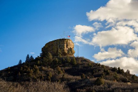 Foto de Un ángulo bajo de roca con la bandera en una colina cubierta por abetos y hierba seca durante un día soleado en Castle Rock, Colorado - Imagen libre de derechos