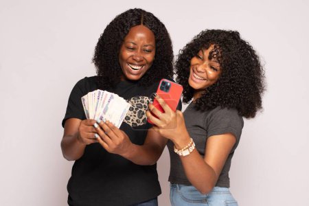 Photo for Two african girls feeling excited holding money and phone - Royalty Free Image
