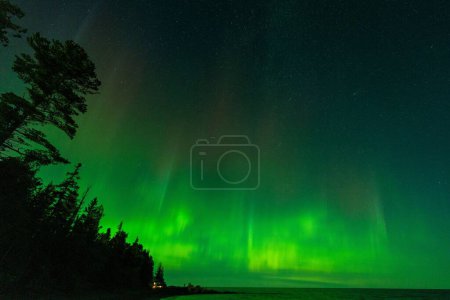 The aurora borealis over the lake surrounded by forest in Keweenaw Peninsula, Michigan