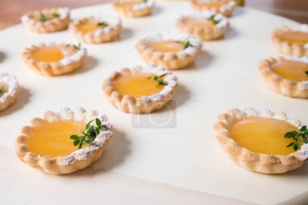 Téléchargez les photos : Un gros plan de nombreuses petites tartes au citron sur une assiette en bois - en image libre de droit