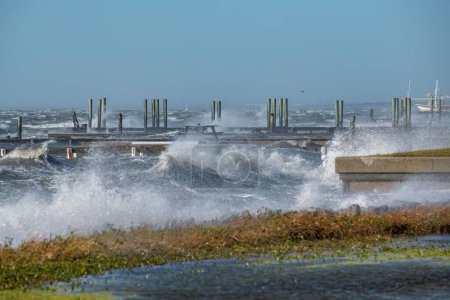 Téléchargez les photos : Un paysage de vagues rugueuses éclaboussant sur des piliers de pierre sur la plage en hiver avec un ciel bleu - en image libre de droit