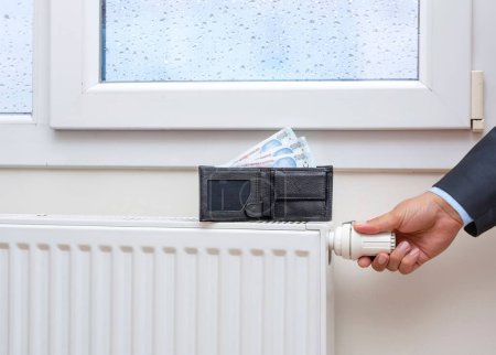 Foto de La mano de un hombre ajustando la temperatura del radiador bajo la ventana - Imagen libre de derechos
