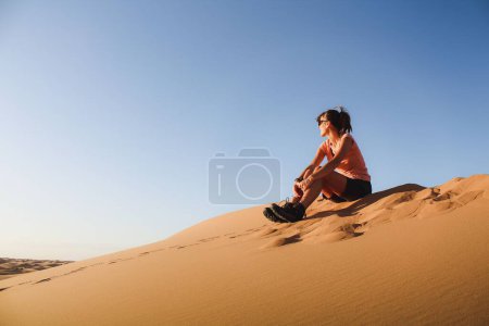 Foto de Una mujer caucásica sentada en la arena en un desierto - Imagen libre de derechos