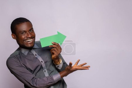 Téléchargez les photos : Excité homme africain tenant et flèche pointant sur le côté - en image libre de droit