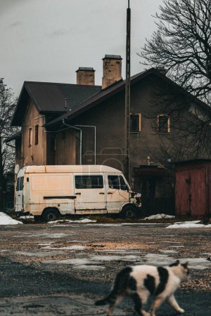 Photo for A vertical shot of the gray concrete house with a small garage and a white van surrounded by bare trees - Royalty Free Image