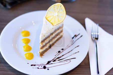 Téléchargez les photos : Un gros plan d'un morceau de gâteau crémeux servi avec de l'orange sur le dessus dans un café - en image libre de droit