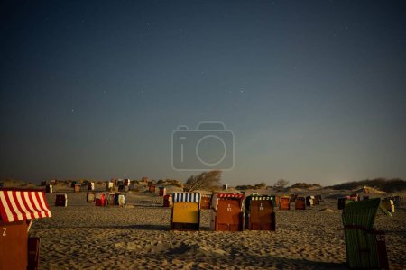 Téléchargez les photos : Plusieurs chaises longues fermées sur le sable d'une côte sous le ciel étoilé bleu la nuit - en image libre de droit