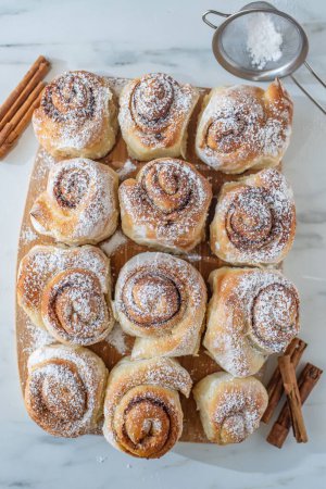 Photo for A vertical top view of tasty cinnamon buns on a wooden dock with sugar powder on them - Royalty Free Image