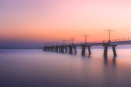 Foto de Un puente sobre un lago tranquilo durante una colorida puesta de sol - Imagen libre de derechos