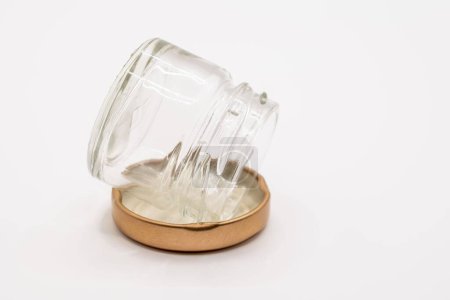 Foto de Primer plano de un pequeño frasco de vidrio de reserva de mermelada transparente vacía con una tapa de metal atornillada de color bronce - Imagen libre de derechos