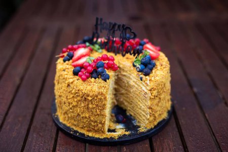 Photo for A closeup of an appetizing birthday cake with berries and a birthday decoration on top missing a slice - Royalty Free Image