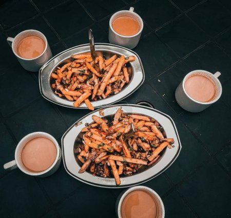 Téléchargez les photos : Les pommes de terre rôties avec des ingrédients sur des bols et des tasses de thé au lait sur une table - en image libre de droit