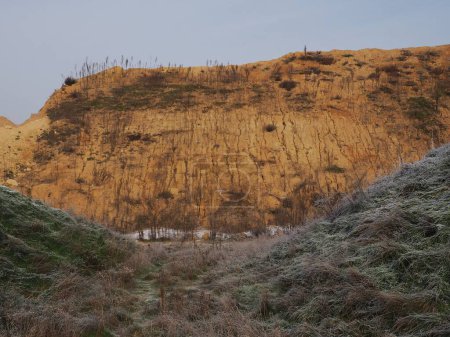 Foto de Una montaña erosionada y un valle con hierba congelada bajo el cielo azul - Imagen libre de derechos