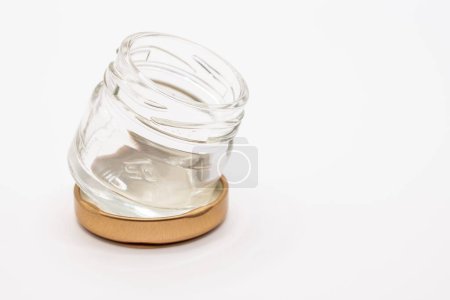 Foto de Primer plano de un pequeño frasco de vidrio de reserva de mermelada transparente vacía con una tapa de metal atornillada de color bronce - Imagen libre de derechos